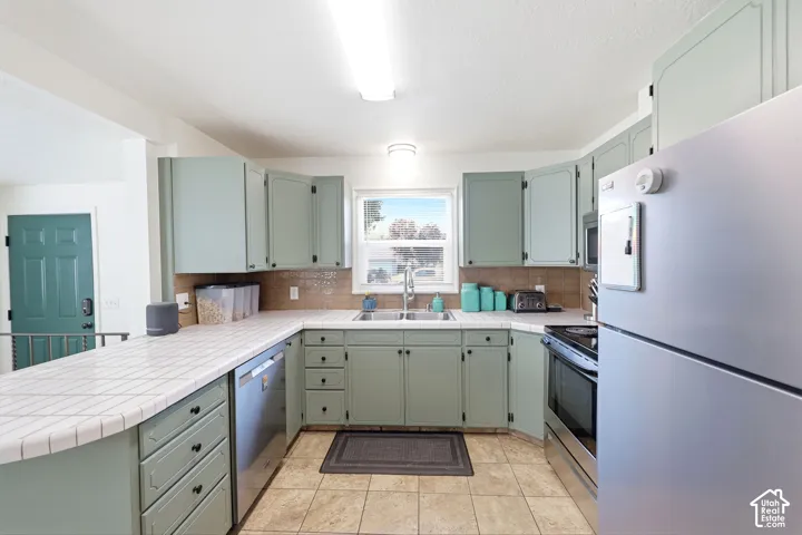 Kitchen featuring light green cabinetry, white tiled countertops, and a tiled backsplash