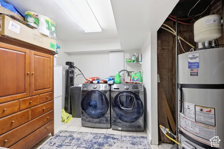 Tiled utility space featuring a water heater, water softener system, and fluorescent overhead lighting