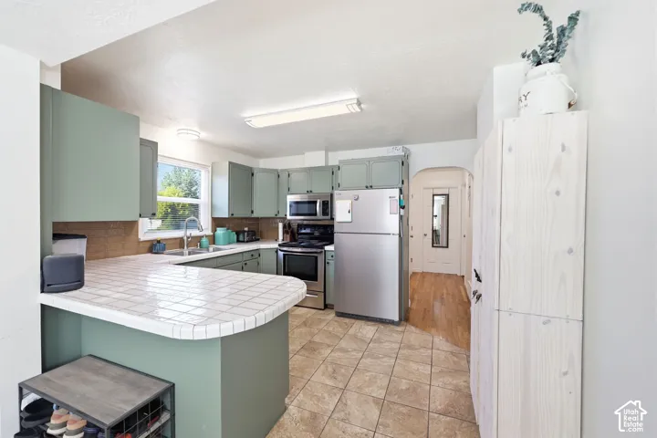 Kitchen featuring sage green cabinetry, tiled countertops, and stainless steel appliances