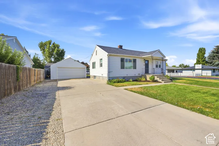 White siding residence featuring a covered front porch with iron railings, a concrete driveway, a detached garage, and a gravel side yard