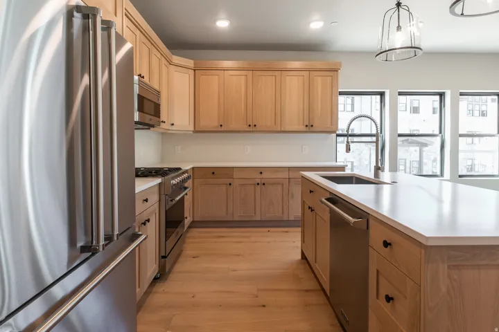 Contemporary kitchen featuring light wood cabinetry, stainless steel appliances, a center island with an undermount sink, and recessed lighting