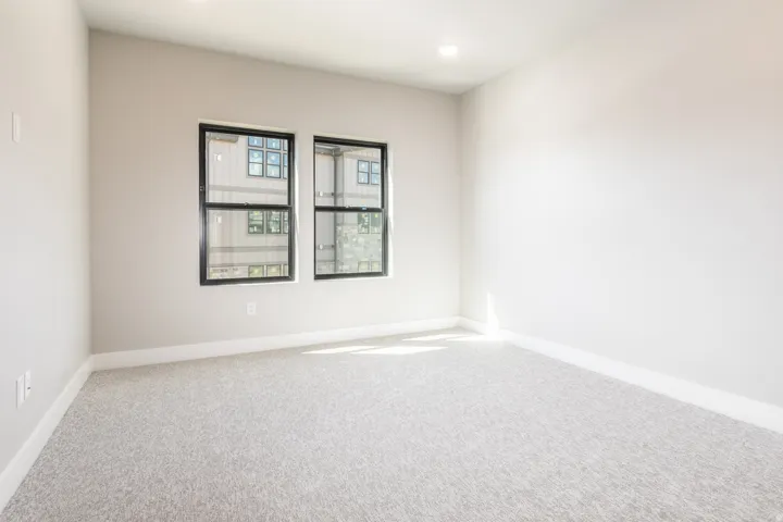 Bright interior room with two black-framed windows, recessed lighting, neutral wall paint, white baseboards, and light-colored carpet flooring