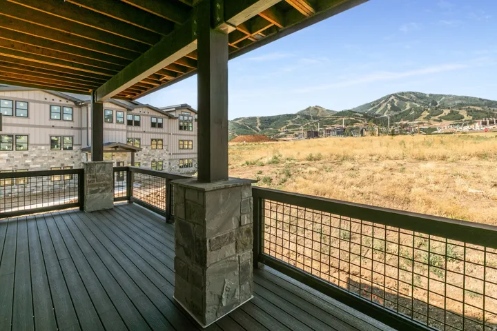 Covered outdoor deck with dark wood-finish flooring, stone-clad pillars, and a metal grid railing