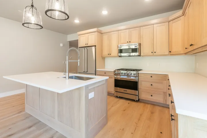 Modern kitchen featuring light wood-finish cabinetry, stainless steel appliances, and a central island with an undermount sink