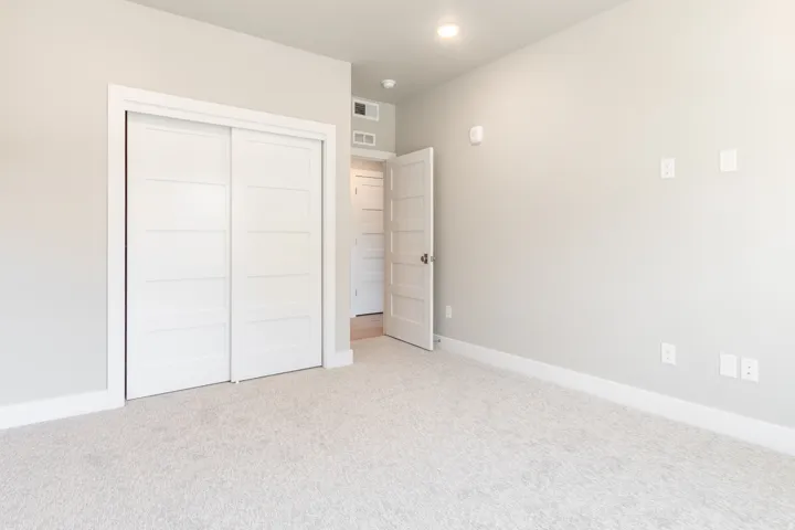 Neutral-toned room featuring light gray walls, plush carpeting, white baseboards, and a white sliding closet door with horizontal paneling