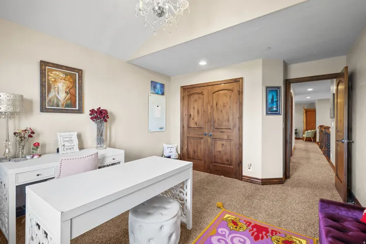 Bedroom or office with vaulted ceiling room featuring natural wood double doors, light tan walls, and carpeted flooring