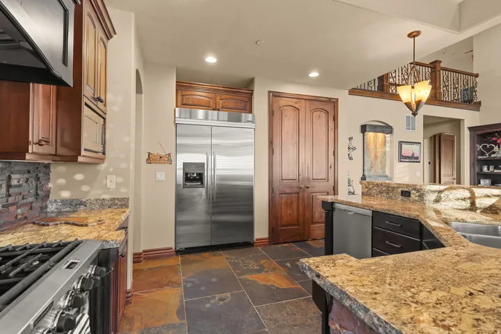 Kitchen featuring custom cabinetry, stainless steel appliances, granite countertops, and slate tile flooring