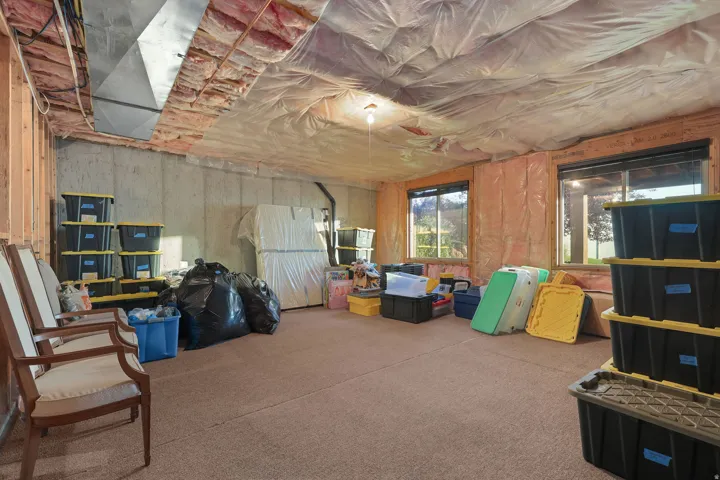 Unfinished basement space featuring exposed concrete walls, wood framing, insulation, and two windows