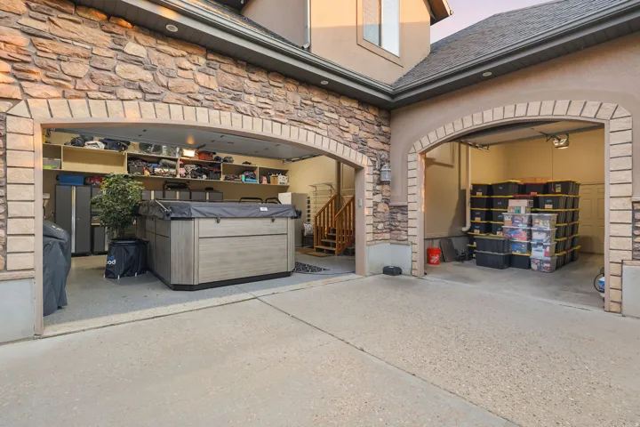 Multi-car garage featuring a large swim spa, built-in storage shelving, a finished concrete floor, and a staircase with wood railings