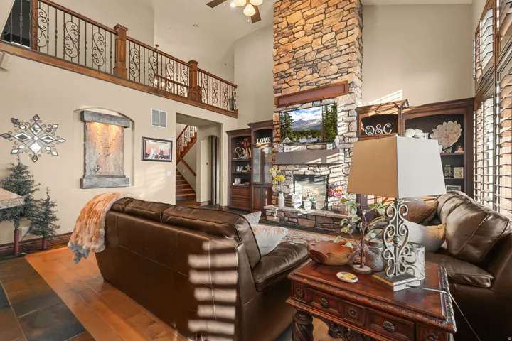 Great room featuring a floor-to-ceiling stone fireplace, built-in shelving, high vaulted ceilings, and a second-story balcony with decorative metal railing