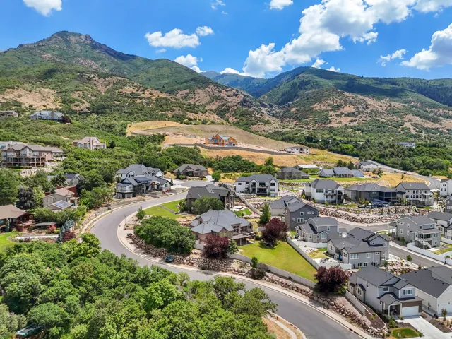 Expansive residential development featuring a curving street, established homes with mature landscaping, and new construction, all set against a mountainous backdrop