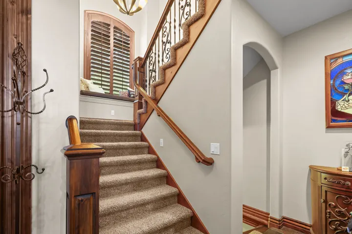 Carpeted staircase going to the upper-level, featuring a wood newel post and handrail, wrought iron balusters, and a built-in window seat with wood shutters