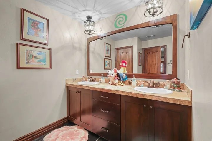 Dual vanity featuring integrated sinks, bronze-finish faucets, a large framed mirror, and two overhead light fixtures