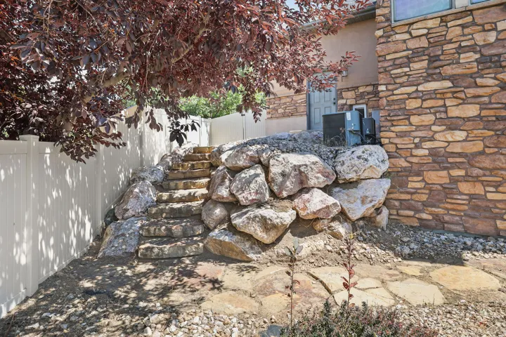 Stone retaining wall with integrated stone steps going to backyard, and bordered by a vinyl fence