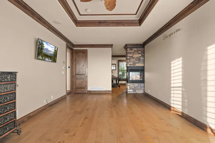 Spacious room featuring wood-finish flooring, a stone-clad fireplace, and an intricate tray ceiling