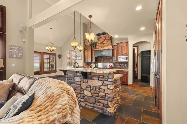 Kitchen featuring a stone-clad island with a granite countertop, rustic wood cabinetry, and a stone-accented range hood