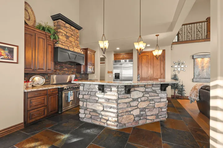 Gourmet kitchen featuring a stone-clad island with granite countertop, stainless steel appliances, wood-finish cabinetry, and slate tile flooring