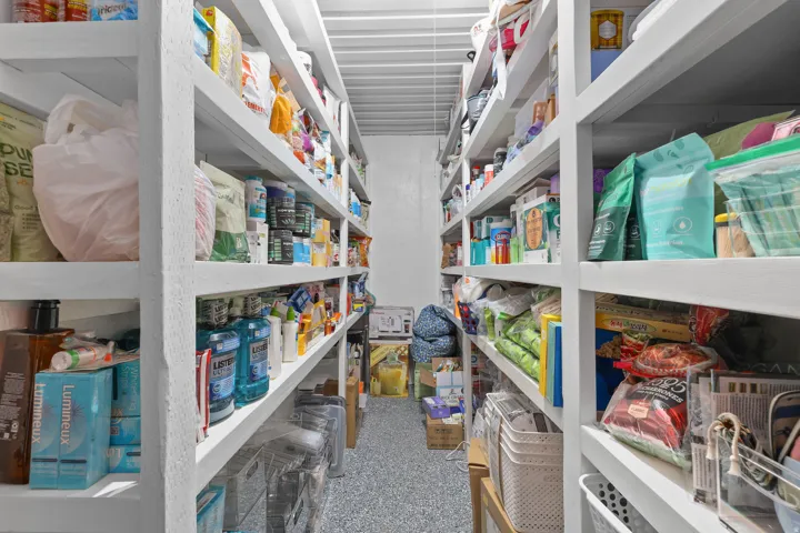 Dedicated storage room featuring extensive built-in shelving, concrete flooring, and ample overhead lighting