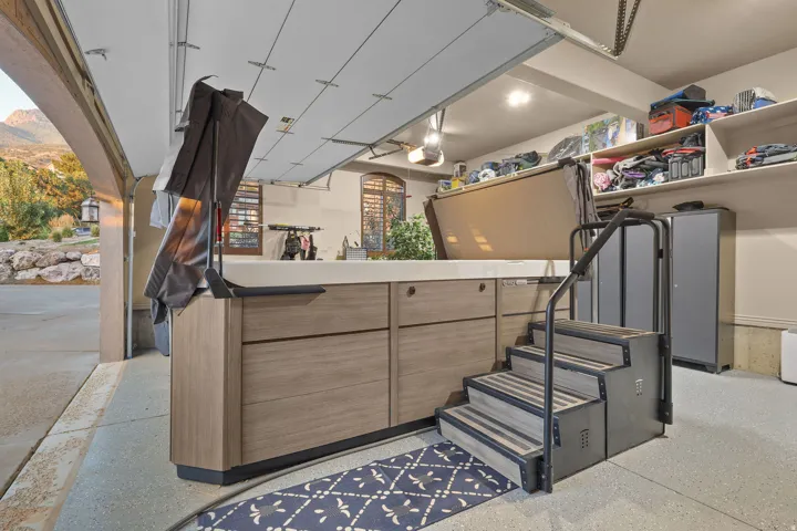 Spacious garage featuring a concrete floor, built-in storage shelving, and a large built-in swim spa with steps and handrails