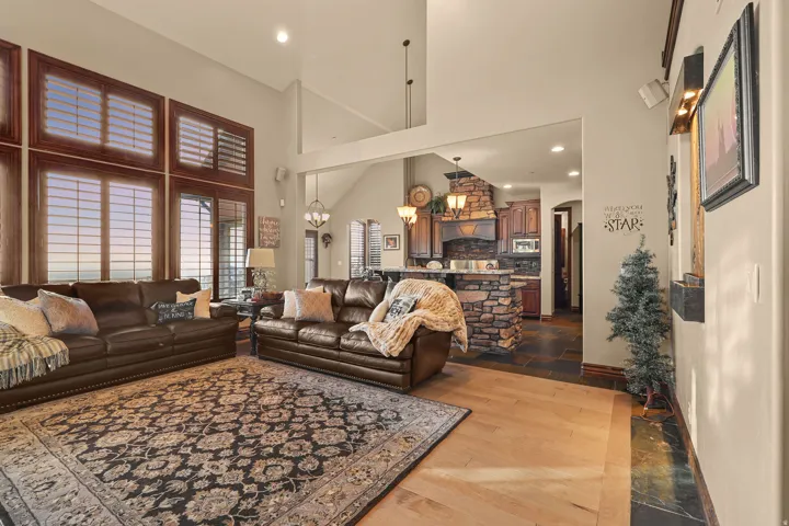 Open-concept living space with vaulted ceilings, large windows featuring wood shutters, and  wood-finish flooring