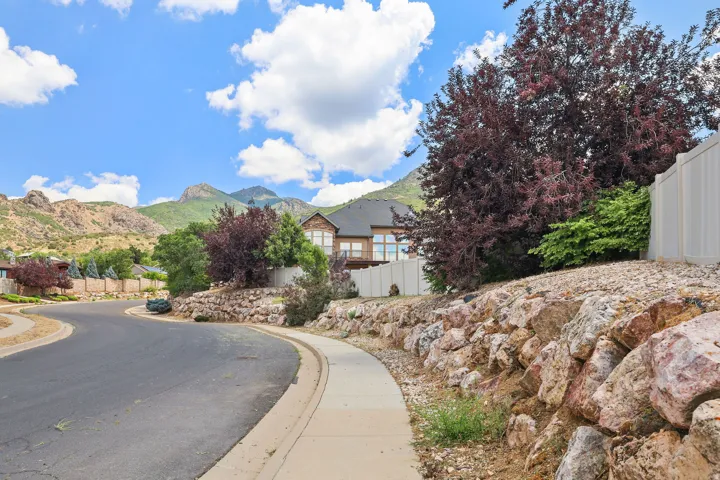 Stone retaining wall featuring vibrant foliage, a paved sidewalk, and mountain scenery