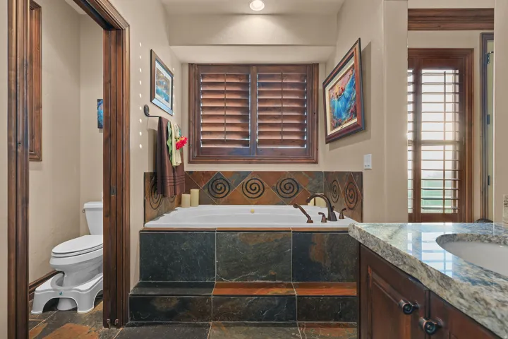 Soaking tub with bronze fixtures, surrounded by slate tile with decorative accents