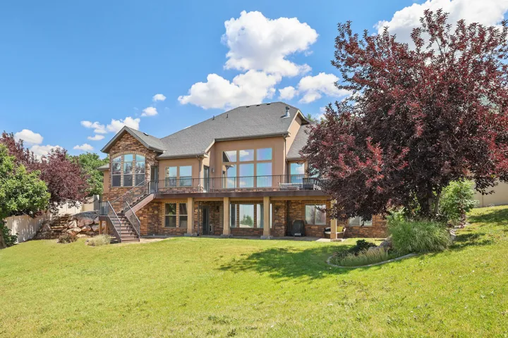 Expansive rear exterior featuring a stone and stucco finish, a second-story deck with metal railings, and a walk-out lower level