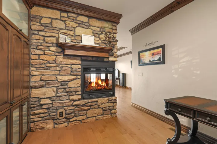 Stacked stone fireplace with a wood mantel, glass-fronted insert, and hardwood-finish flooring