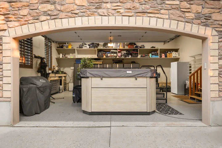 Stone veneer archway entry to a garage space featuring a light wood-finish spa with steps and handrail, built-in shelving, and light gray flooring
