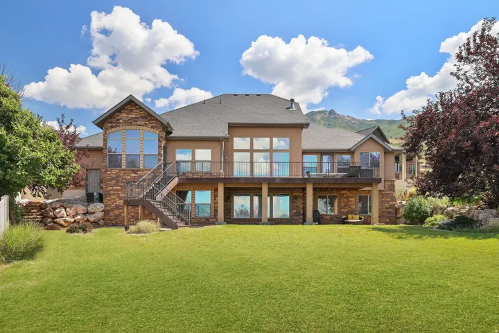 Brick and stone exterior with multi-level architecture featuring expansive windows, a covered deck with metal railings, and a professionally landscaped yard