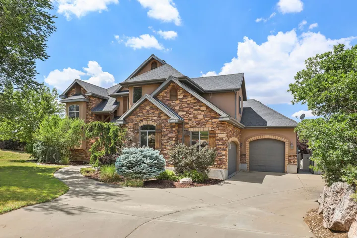 Stone and stucco exterior featuring a multi-gabled roofline, arched garage entry, and decorative window shutters