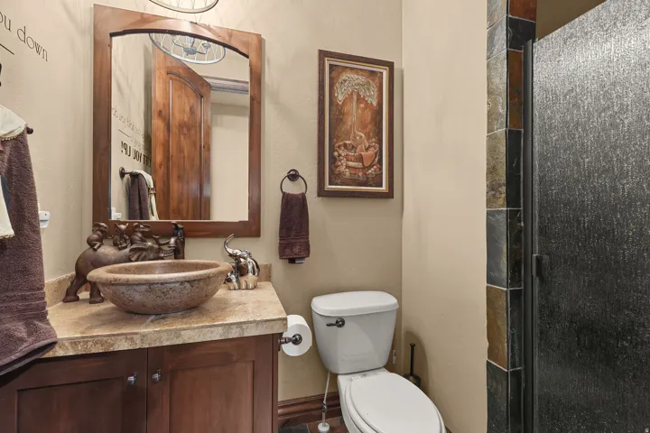 Bathroom featuring a stone vessel sink, wood vanity with cabinet storage, framed mirror, and a shower with textured glass and slate-style tile surround
