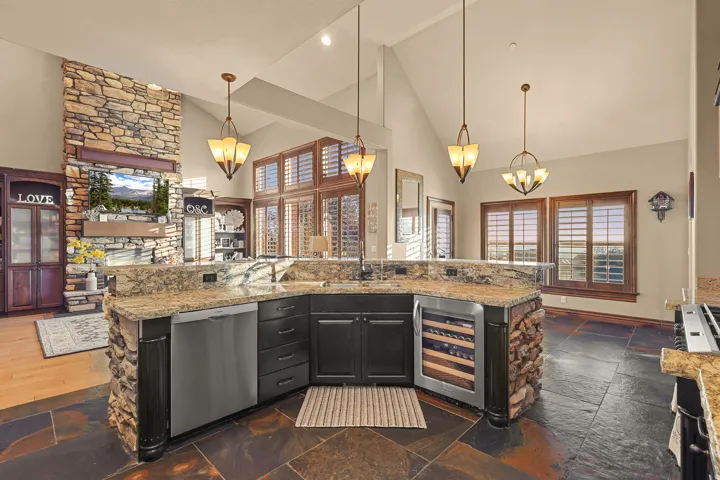 Kitchen island featuring a stone base, granite countertops, an undermount sink, and a built-in beverage refrigerator