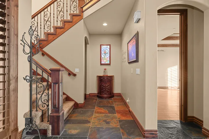 Foyer featuring multi-toned slate flooring, a wood staircase with carpeted treads and ornate wrought iron balusters, and an arched doorway leading to a room with wood-finish flooring