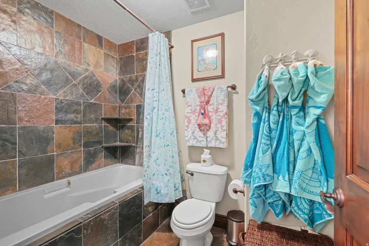 Bathroom featuring a combination bathtub and shower with natural stone tile surround and built-in corner shelving