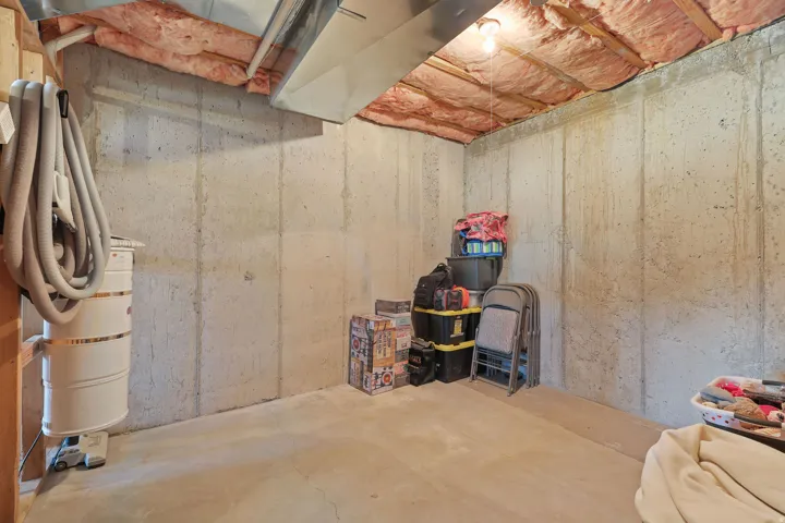 Unfinished basement featuring concrete walls, exposed insulation, overhead lighting, and an exposed duct system