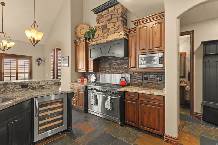 Gourmet kitchen featuring a stone-clad range hood, stainless steel professional-grade range, wood cabinetry, granite countertops, and slate tile flooring