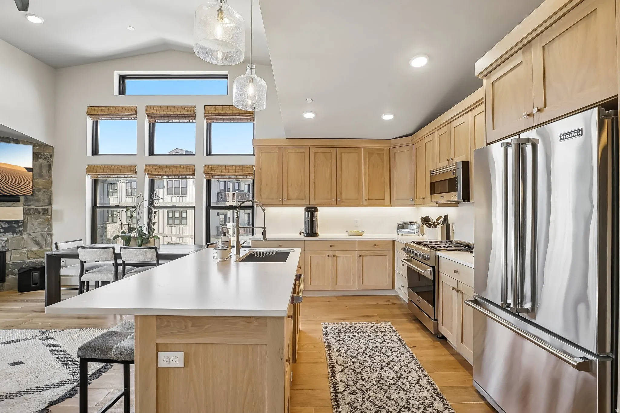 Open-concept kitchen featuring light wood cabinetry, stainless steel appliances, a center island with a sink, and pendant lighting