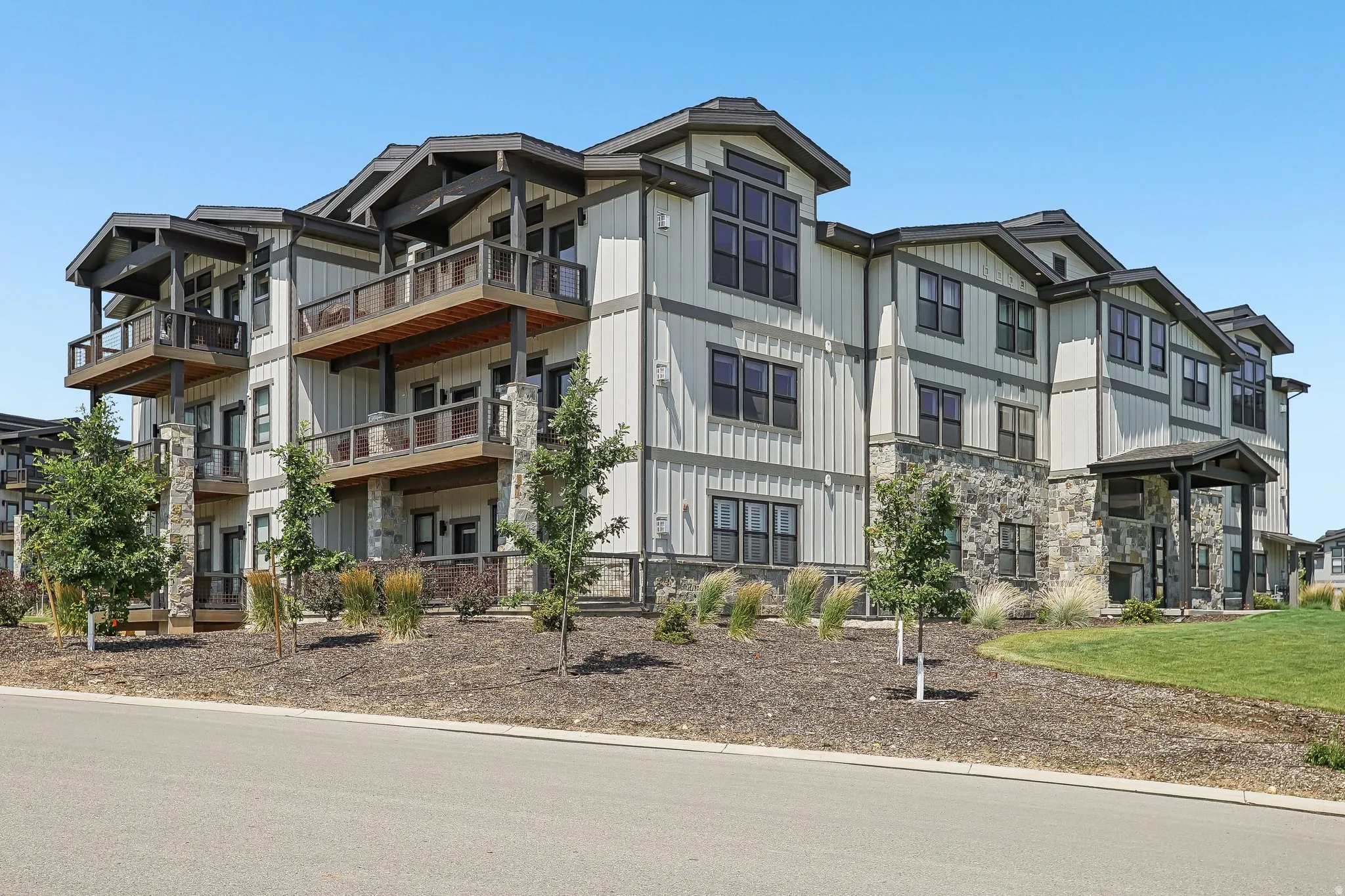 Multi-story residential building featuring board and batten siding, stone facade, covered entry, and individual balconies with wooden railings