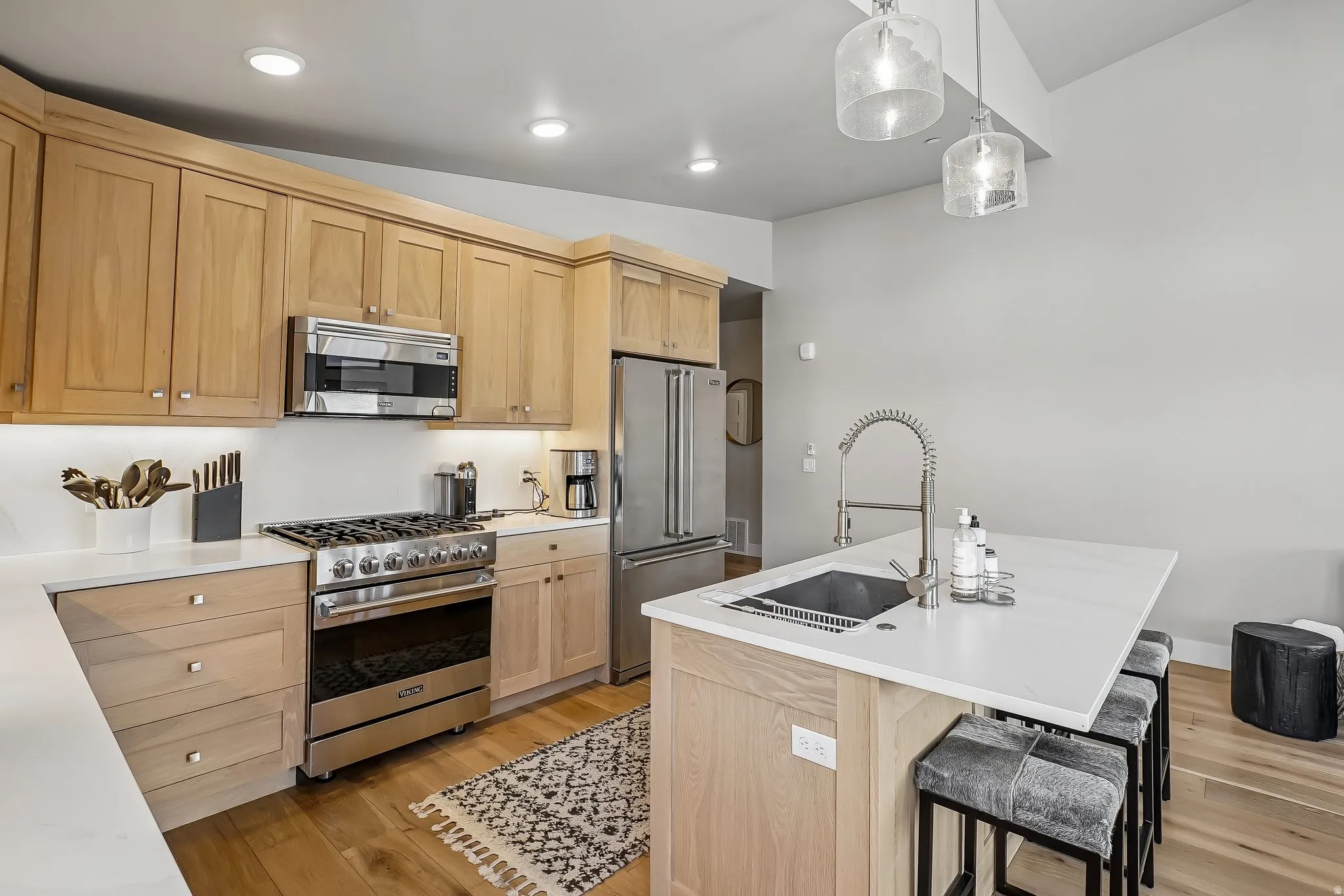Open-concept kitchen featuring wood-finish cabinetry, stainless steel appliances, a center island with an undermount sink, and recessed lighting