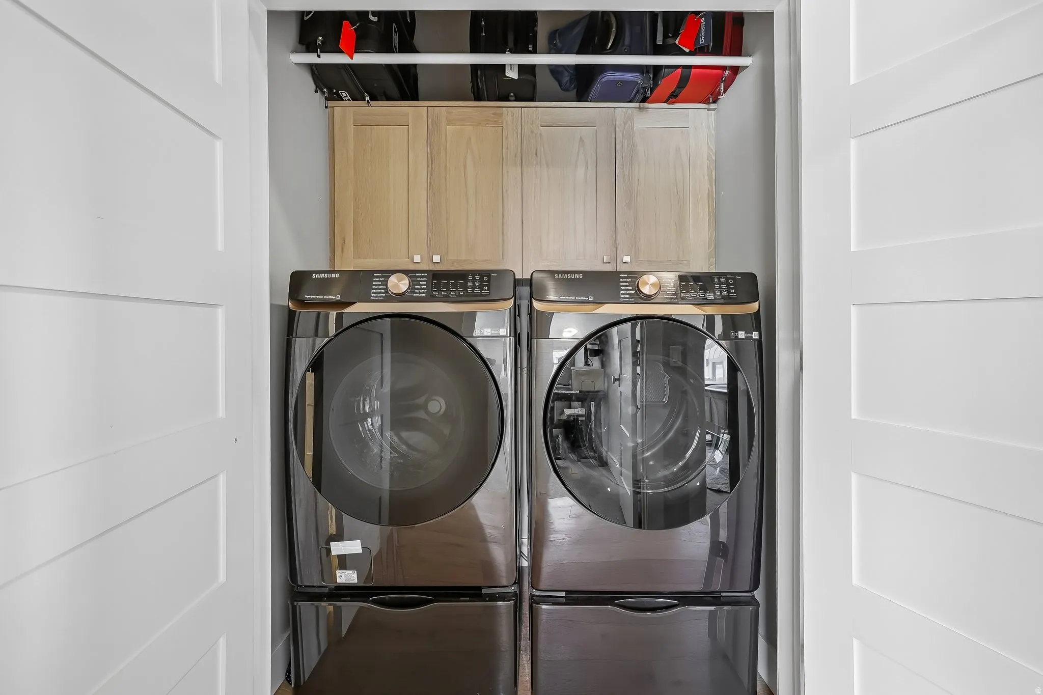 Dedicated laundry area featuring a front-loading washer and dryer set on pedestals, complemented by two-door upper cabinetry and an open shelf for additional storage