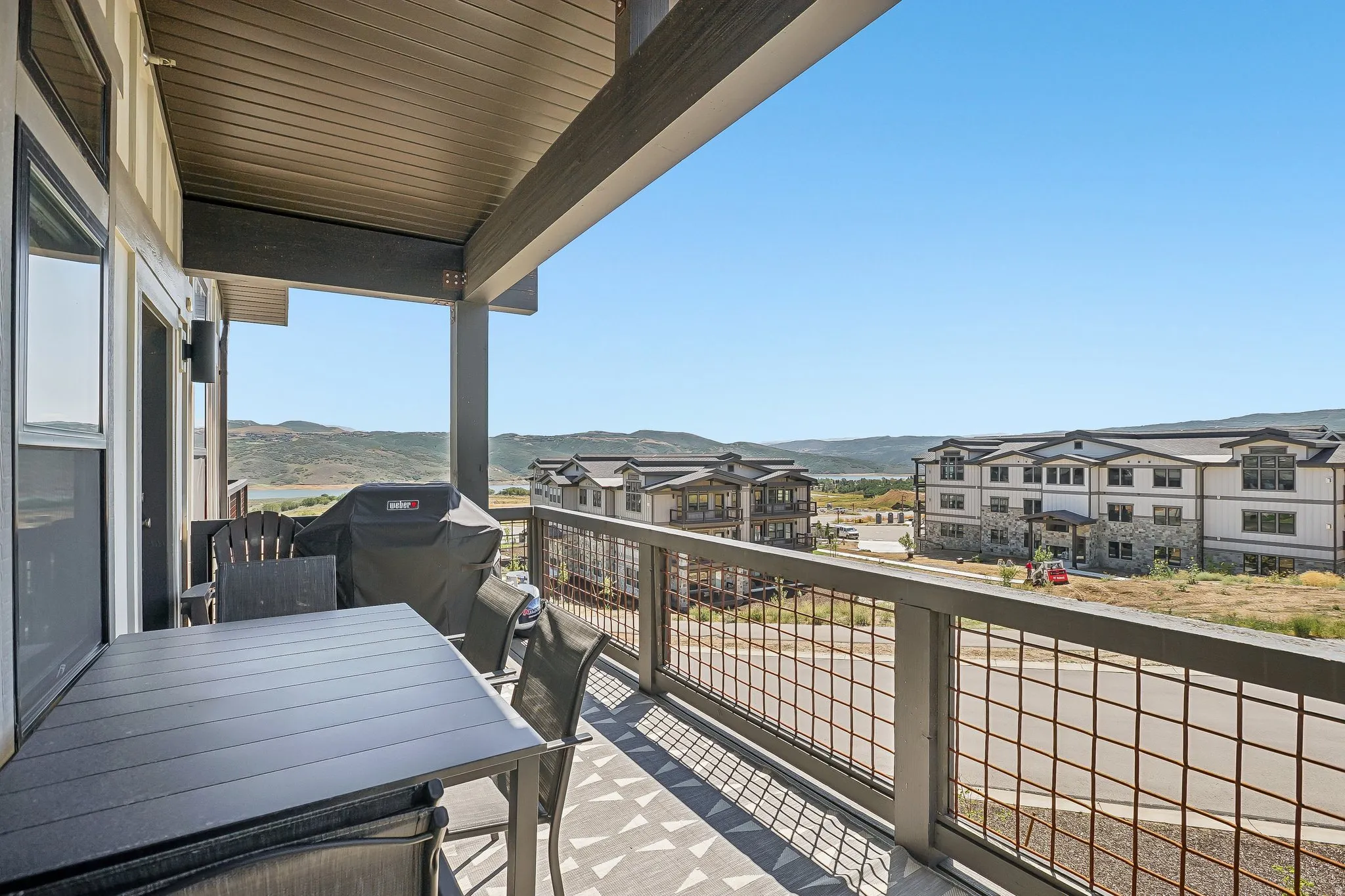 Covered outdoor balcony featuring metal railing with grid infill, wood-finish flooring, and exterior wall lighting