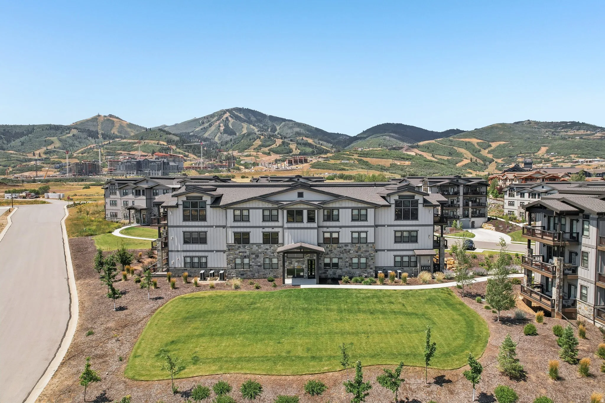 Multi-story residential building with a stone and siding exterior, featuring multiple balconies and a large central green space