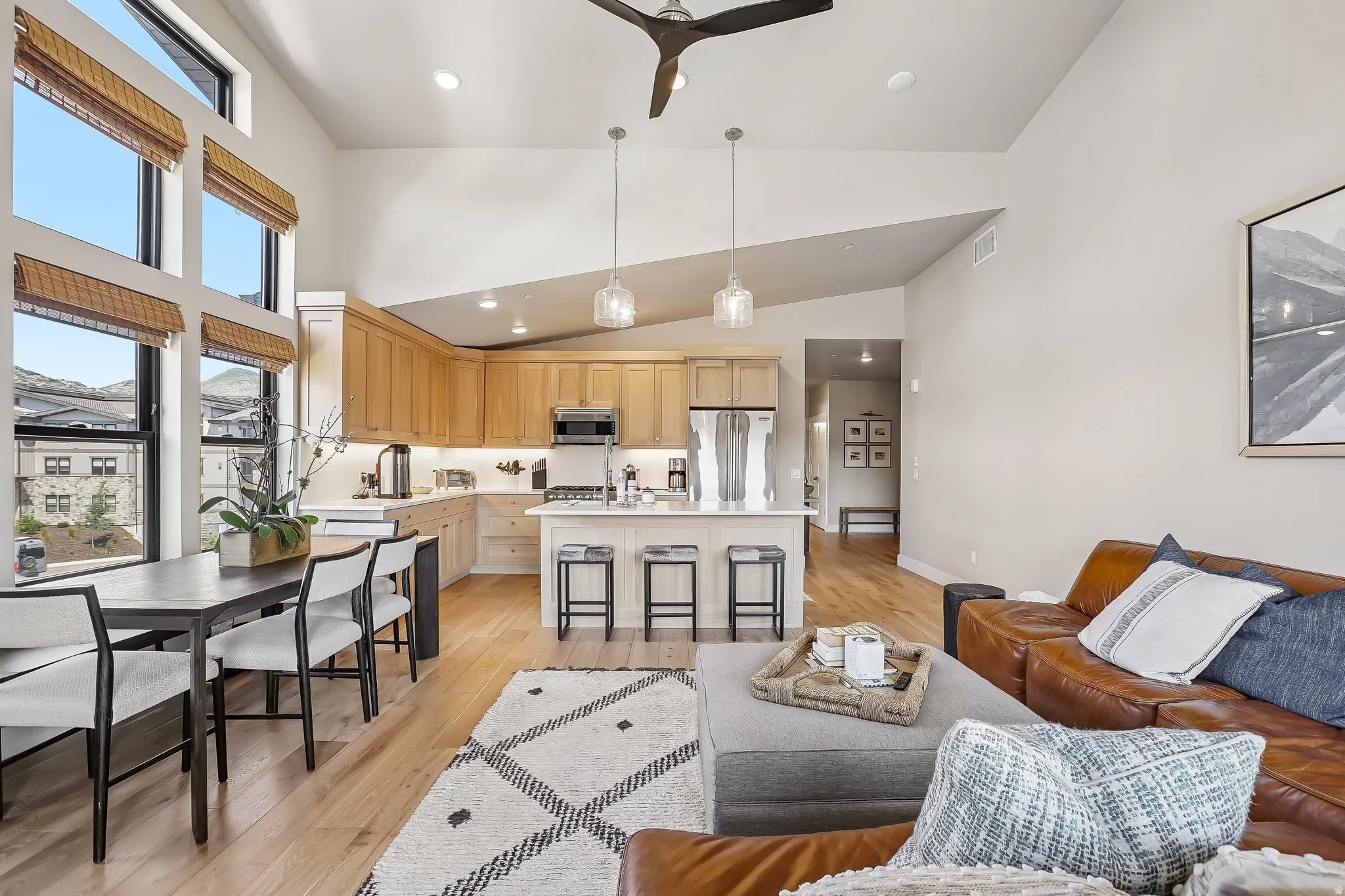 Vaulted ceilings complement the open-concept living area, featuring a kitchen with light wood cabinetry, white countertops, and stainless steel appliances