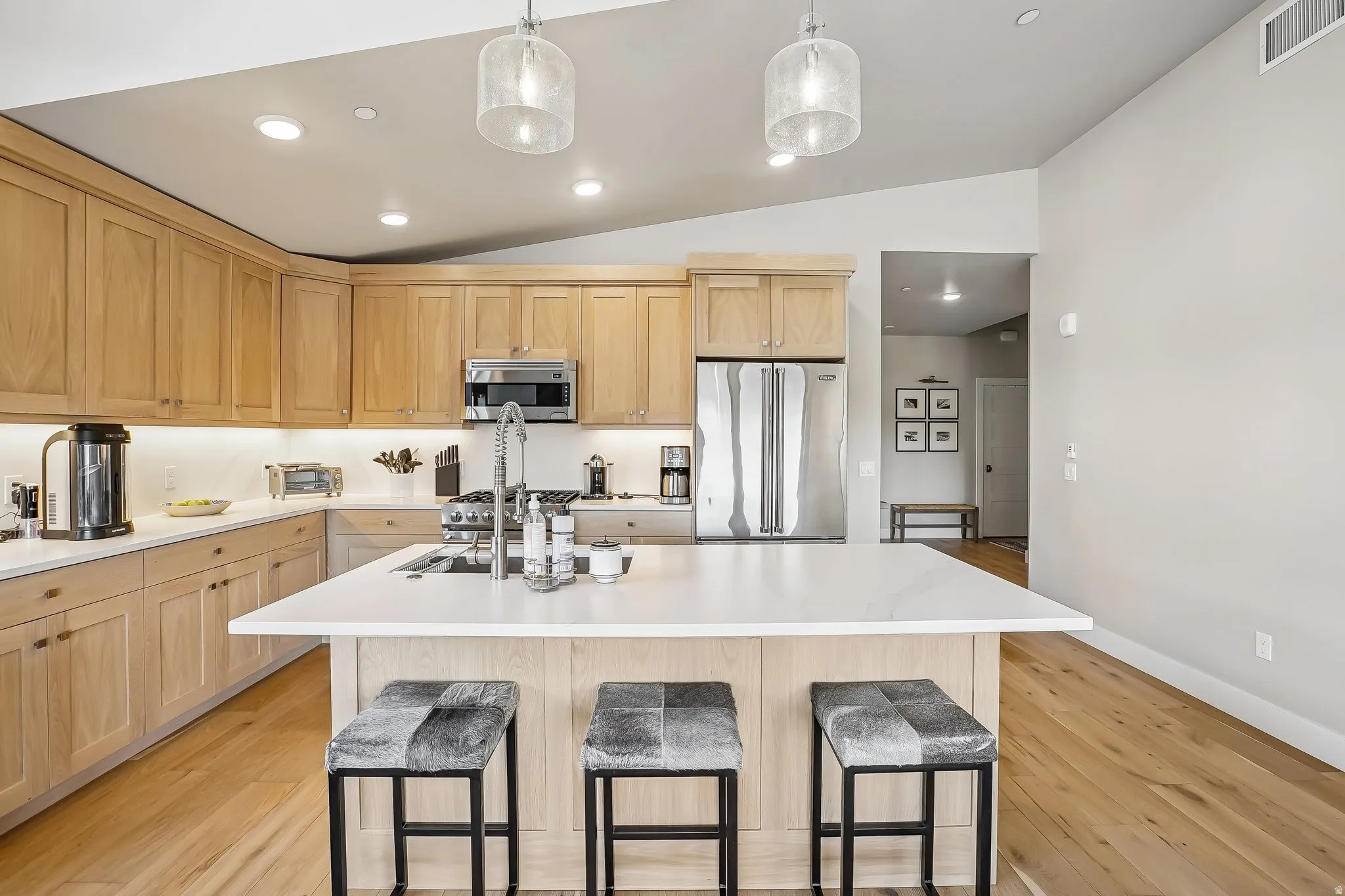 Modern kitchen featuring light wood cabinetry, a central island with countertop seating, stainless steel appliances, and wood-finish flooring