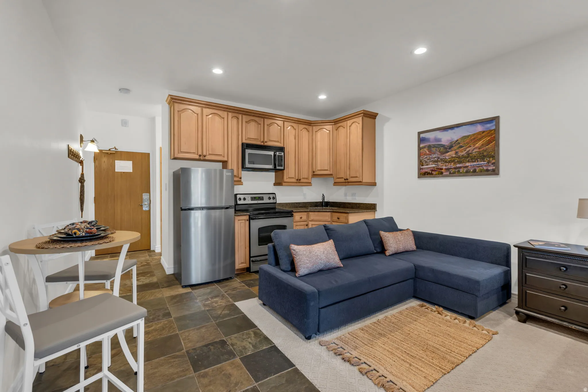 Compact kitchen area featuring wood cabinetry, stainless steel appliances, and dark stone countertops