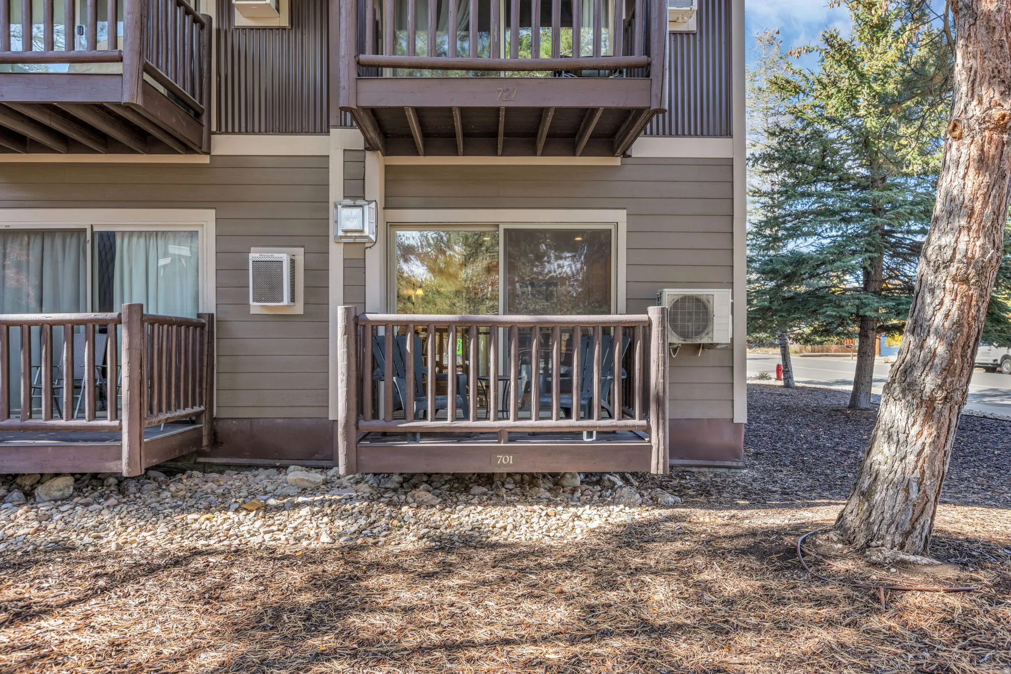 Dual ground-level patios with wood railings and dark brown siding