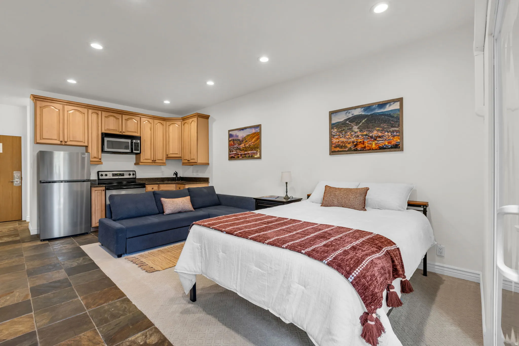 Open-concept living space with a full kitchen, featuring wood cabinetry, stainless steel appliances, and a dark countertop