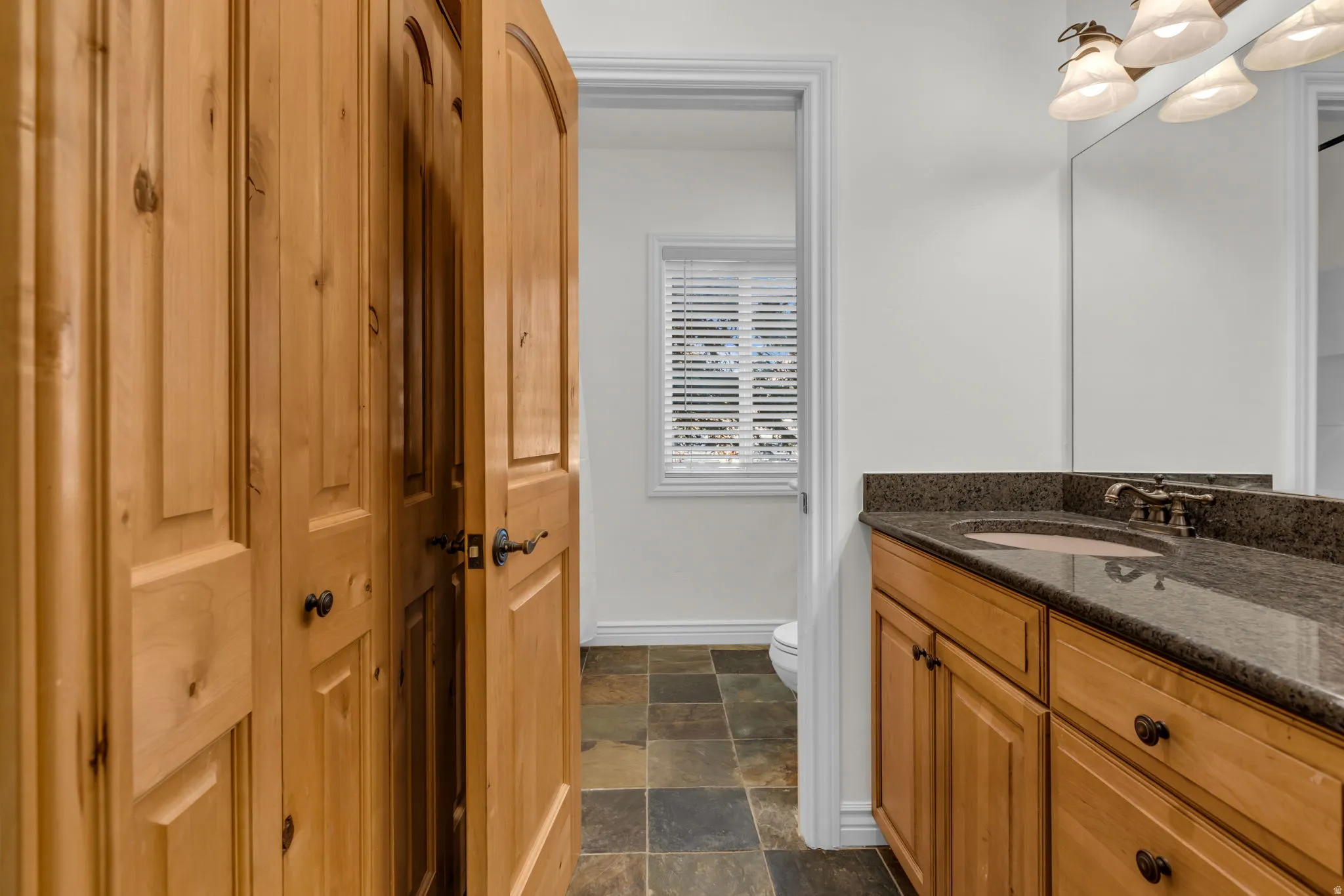 Bathroom vanity featuring a granite countertop with an integrated sink, bronze-finish faucet, and warm wood-finish cabinetry