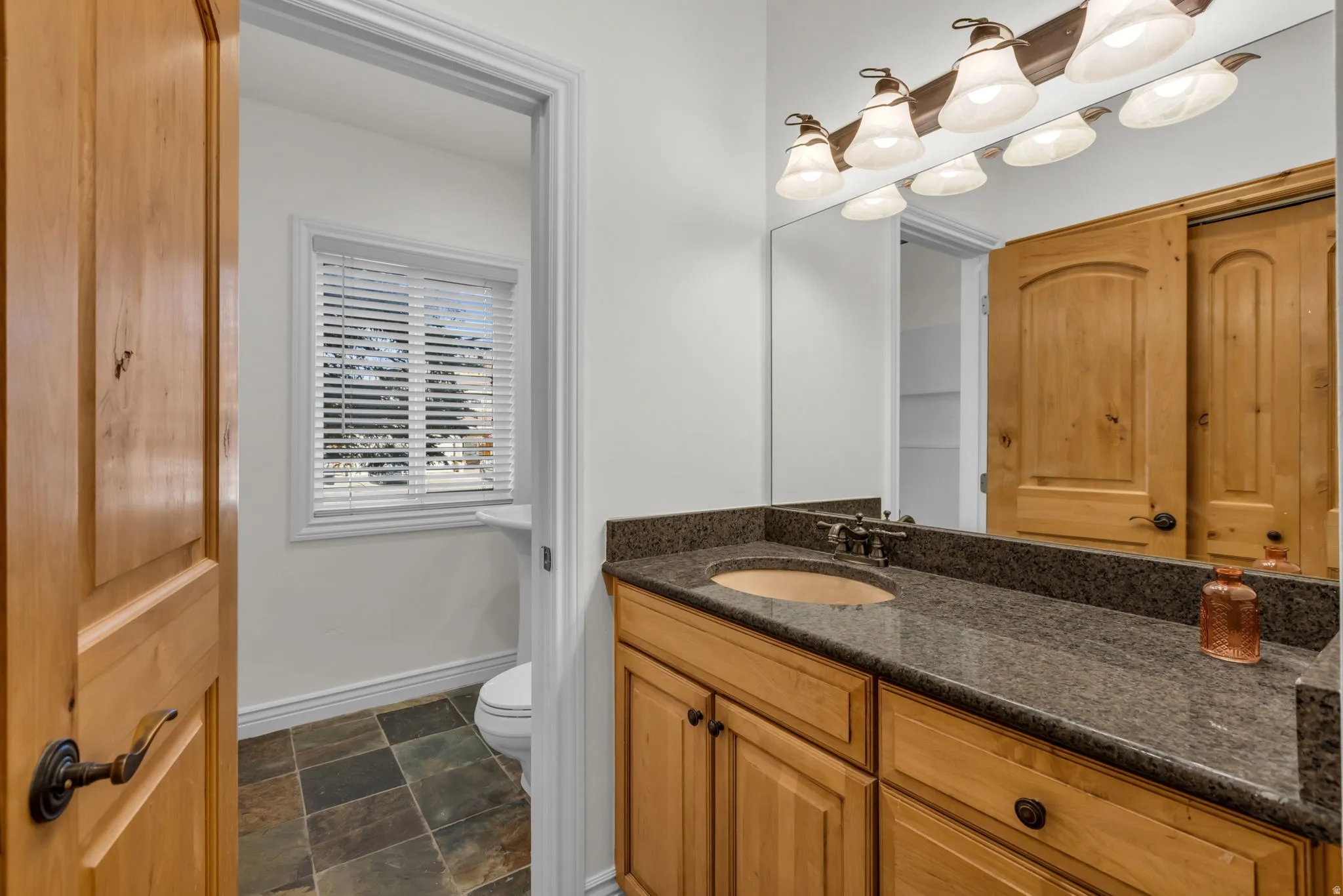 Bathroom featuring a granite countertop vanity with a copper sink, wood-finish cabinetry, a large mirror, and slate tile flooring